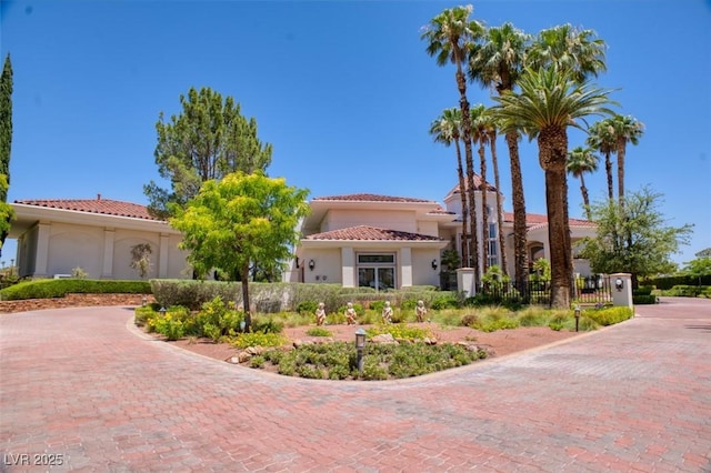 mediterranean / spanish house featuring a tile roof, fence, decorative driveway, and stucco siding