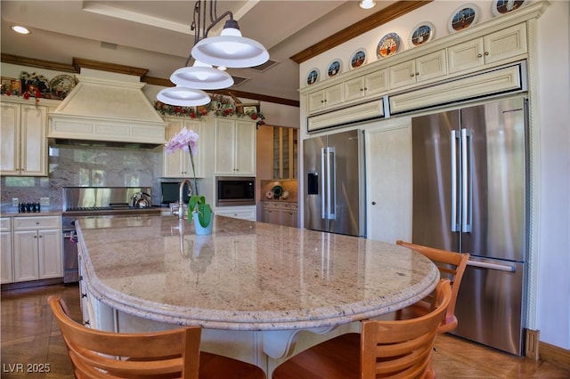 kitchen with a center island with sink, custom range hood, high quality appliances, decorative backsplash, and decorative light fixtures