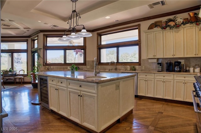 kitchen with a kitchen island with sink, wine cooler, a tray ceiling, sink, and decorative light fixtures