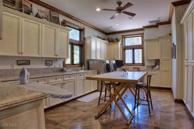 kitchen featuring washer and dryer, cream cabinets, ornamental molding, and light parquet flooring