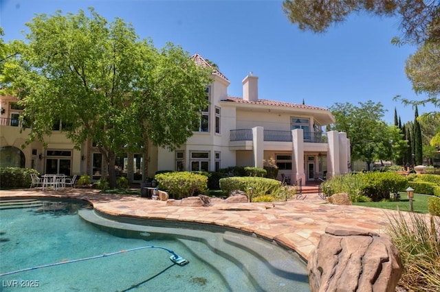 back of house featuring a patio, a chimney, stucco siding, a balcony, and an outdoor pool