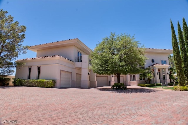 mediterranean / spanish-style home featuring a garage, a tiled roof, decorative driveway, and stucco siding