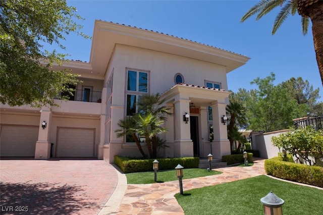 mediterranean / spanish-style home with a garage, decorative driveway, a balcony, and stucco siding