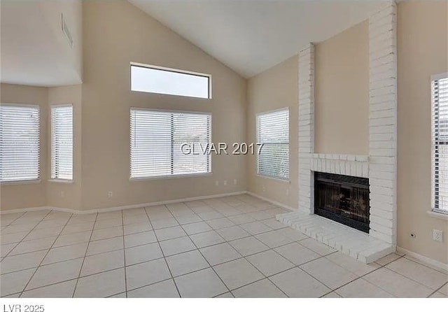 unfurnished living room with a brick fireplace, vaulted ceiling, a wealth of natural light, and light tile patterned floors