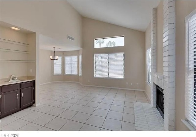 unfurnished living room with light tile patterned flooring, sink, a brick fireplace, and a wealth of natural light