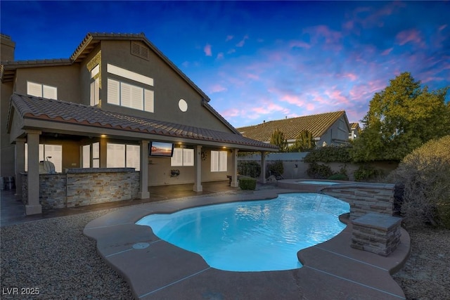 pool at dusk with exterior bar, an in ground hot tub, and a patio area