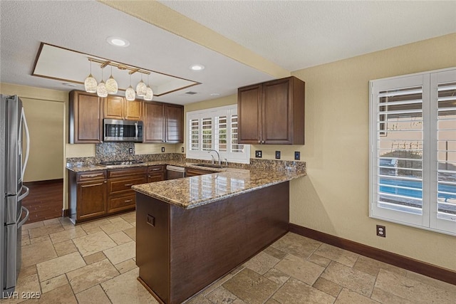 kitchen with sink, kitchen peninsula, decorative backsplash, pendant lighting, and appliances with stainless steel finishes