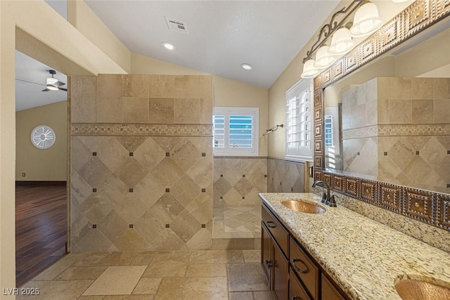 bathroom featuring vaulted ceiling, tiled shower, vanity, tile walls, and ceiling fan