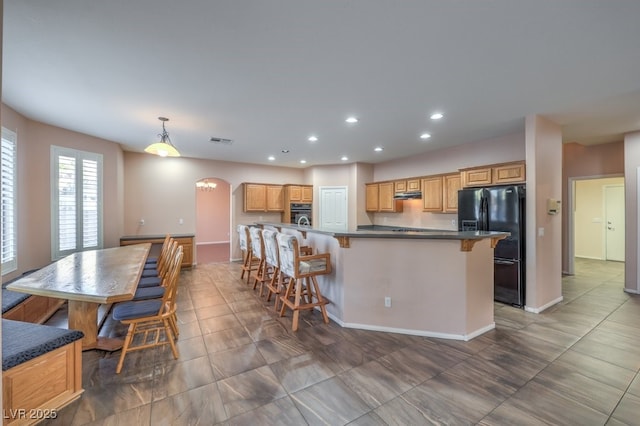 kitchen with black fridge, decorative light fixtures, a center island with sink, and a kitchen breakfast bar