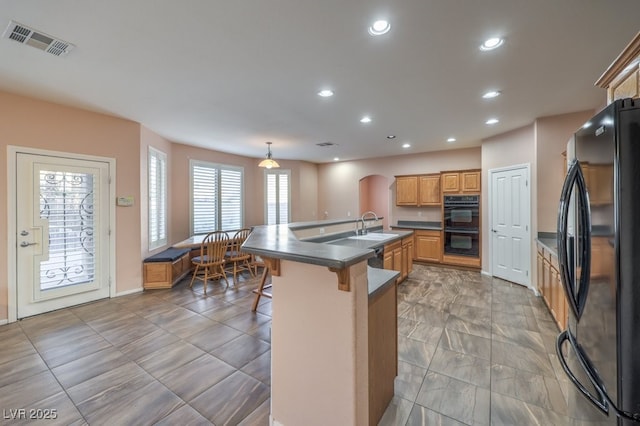 kitchen with pendant lighting, a center island with sink, black appliances, a kitchen bar, and sink