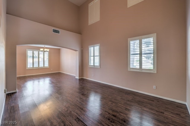 unfurnished room with dark hardwood / wood-style flooring, a towering ceiling, and a chandelier