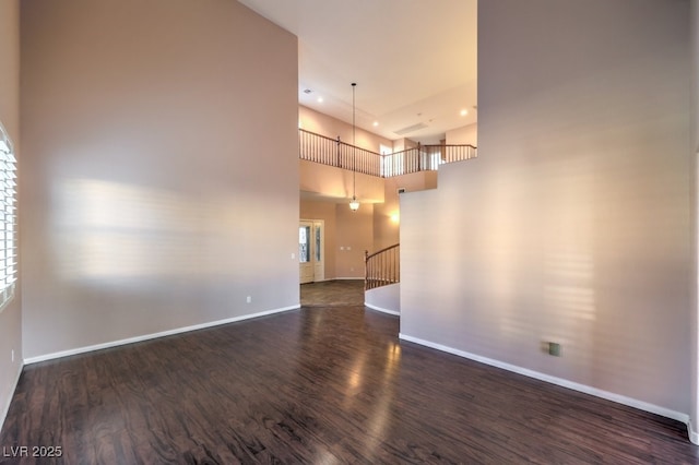 empty room featuring a healthy amount of sunlight, a towering ceiling, and dark hardwood / wood-style floors