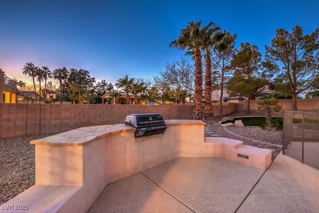 patio terrace at dusk with exterior kitchen and a grill