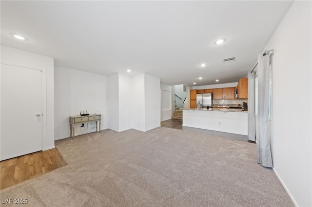 unfurnished living room featuring stairs, visible vents, light colored carpet, and recessed lighting