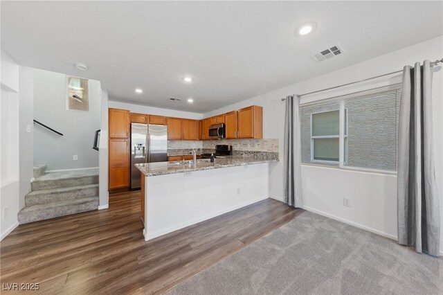 kitchen with light stone counters, kitchen peninsula, wood-type flooring, backsplash, and appliances with stainless steel finishes