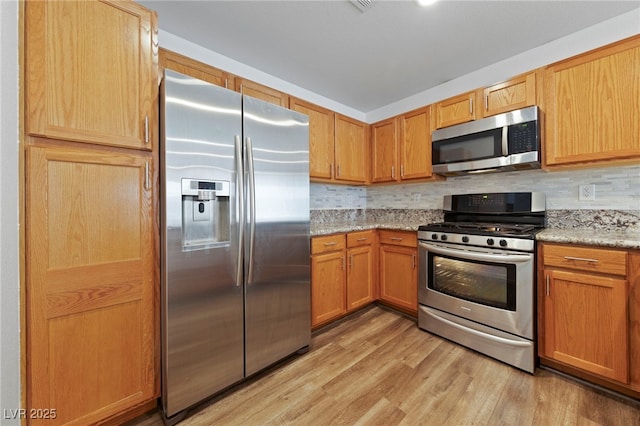 kitchen featuring light wood-type flooring, light stone countertops, appliances with stainless steel finishes, and decorative backsplash