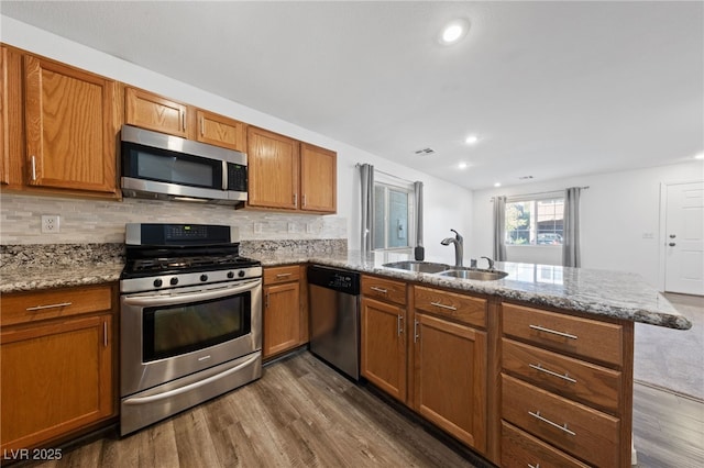 kitchen with sink, stainless steel appliances, light stone countertops, and kitchen peninsula