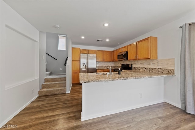 kitchen with stainless steel appliances, kitchen peninsula, sink, light hardwood / wood-style flooring, and backsplash