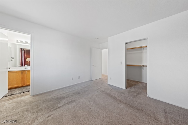 unfurnished bedroom featuring ensuite bath, a spacious closet, a closet, light colored carpet, and sink