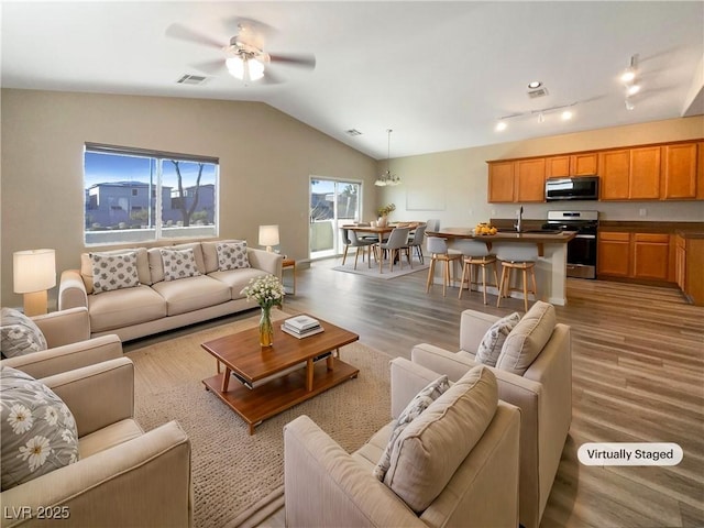 living room featuring ceiling fan with notable chandelier, vaulted ceiling, and light hardwood / wood-style floors