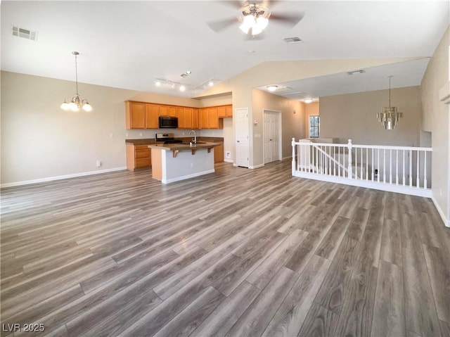 kitchen featuring sink, lofted ceiling, an island with sink, ceiling fan with notable chandelier, and stainless steel range