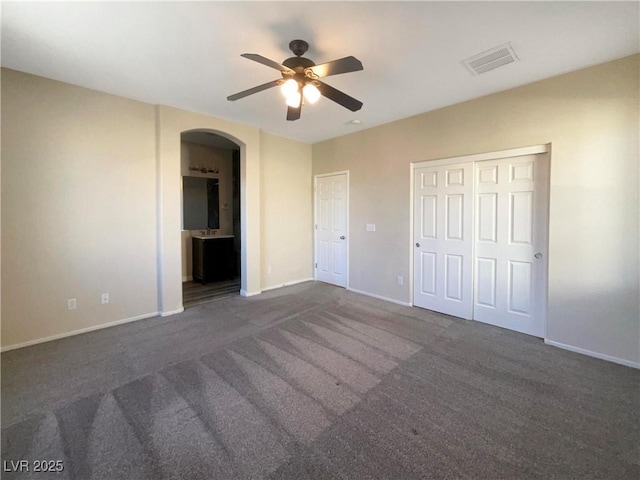 unfurnished bedroom featuring ensuite bath, ceiling fan, and dark colored carpet