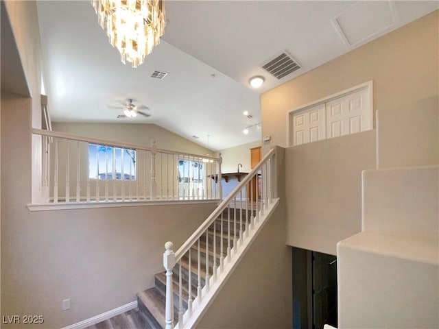 staircase featuring lofted ceiling, ceiling fan with notable chandelier, and wood-type flooring