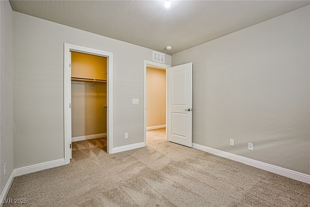 unfurnished bedroom with light colored carpet, a closet, a spacious closet, and a textured ceiling