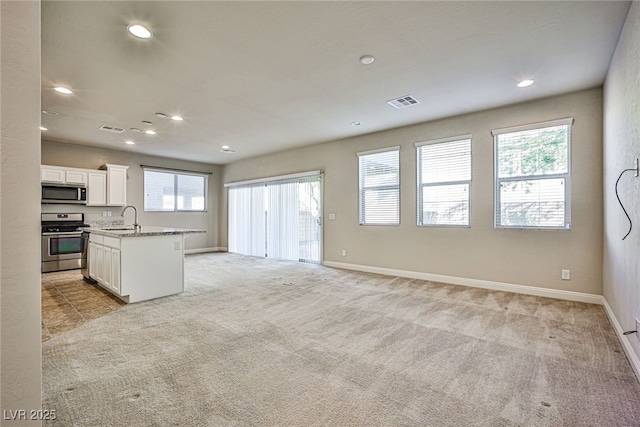 kitchen with stainless steel appliances, sink, white cabinetry, light stone countertops, and a kitchen island with sink