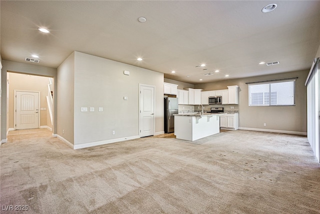 kitchen featuring stainless steel appliances, white cabinetry, a kitchen island with sink, and light carpet