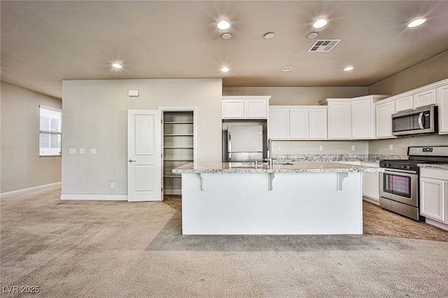 kitchen with stainless steel appliances, a kitchen island with sink, light stone countertops, and a breakfast bar area