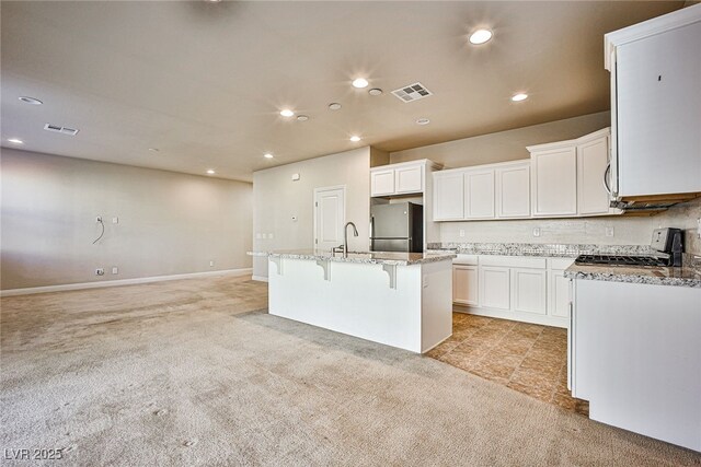 kitchen featuring range, a center island with sink, stainless steel refrigerator, a breakfast bar, and white cabinets