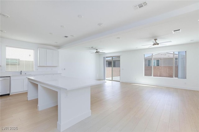 kitchen featuring white dishwasher, white cabinets, a center island, and a wealth of natural light