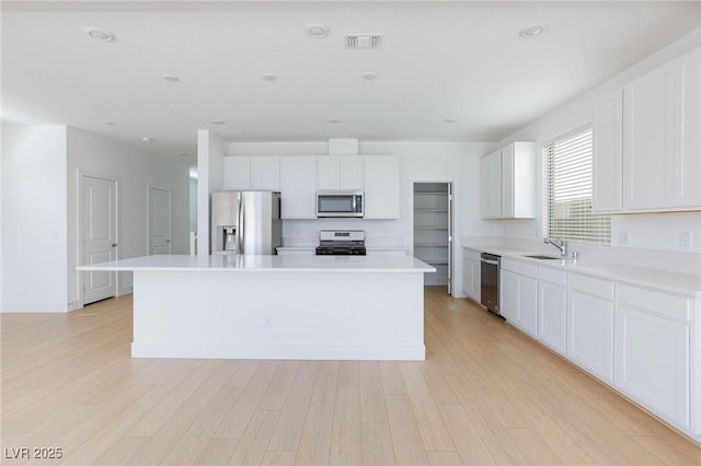 kitchen with appliances with stainless steel finishes, light wood-type flooring, a kitchen island, white cabinets, and sink