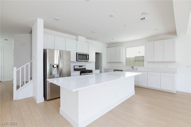 kitchen with sink, white cabinets, a center island, light hardwood / wood-style flooring, and appliances with stainless steel finishes