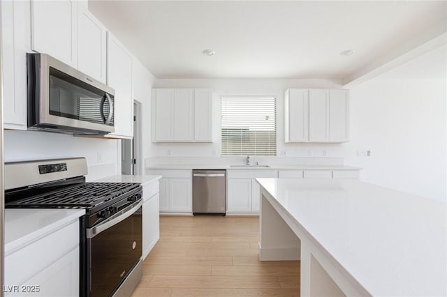 kitchen with appliances with stainless steel finishes, light hardwood / wood-style flooring, white cabinetry, and sink