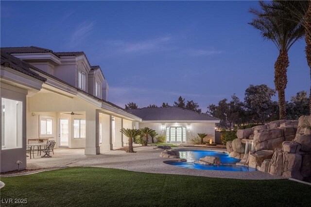 pool at dusk featuring french doors, a yard, ceiling fan, and a patio