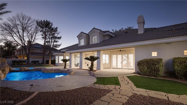 pool at dusk featuring pool water feature, a patio area, and ceiling fan