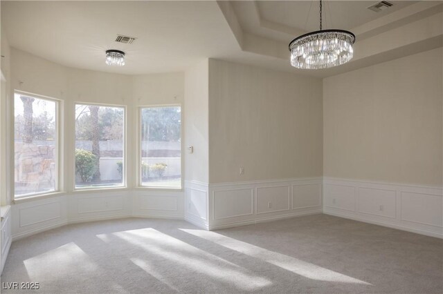 unfurnished dining area with an inviting chandelier, a raised ceiling, and light colored carpet