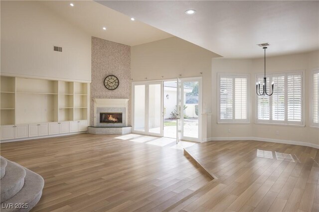 unfurnished living room featuring a large fireplace, a high ceiling, light wood-type flooring, an inviting chandelier, and built in features