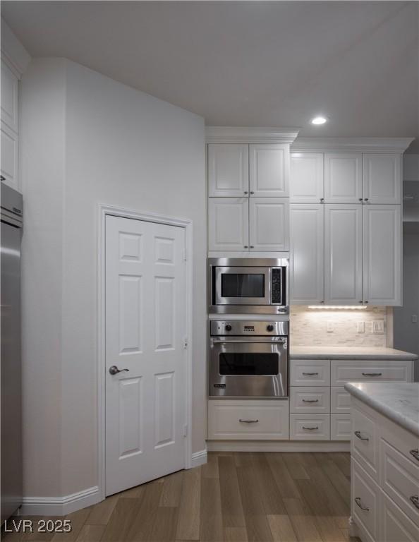 kitchen with stainless steel appliances, white cabinets, tasteful backsplash, and light hardwood / wood-style flooring