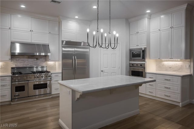 kitchen featuring a center island, built in appliances, pendant lighting, white cabinetry, and range hood