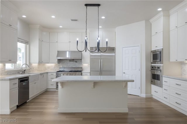 kitchen with wood-type flooring, a center island, built in appliances, white cabinetry, and backsplash