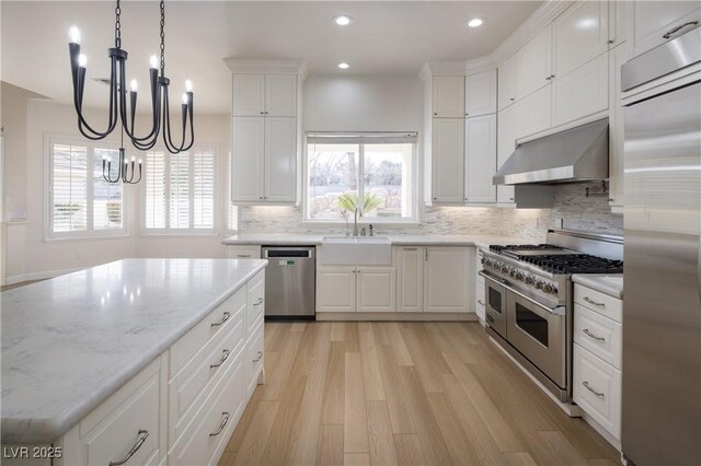 kitchen featuring wall chimney exhaust hood, pendant lighting, white cabinetry, appliances with stainless steel finishes, and sink