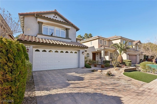 mediterranean / spanish-style home featuring an attached garage, a tile roof, decorative driveway, and stucco siding