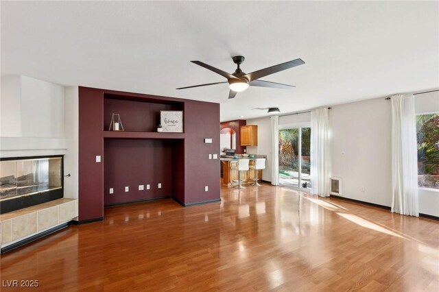 unfurnished living room featuring a fireplace, ceiling fan, hardwood / wood-style flooring, and a wealth of natural light