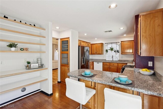 kitchen featuring dishwasher, stainless steel fridge with ice dispenser, kitchen peninsula, dark wood-type flooring, and a kitchen bar