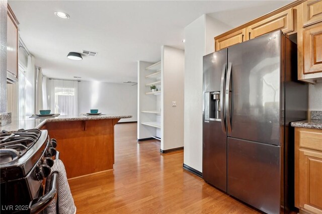 kitchen with stainless steel appliances, light wood-type flooring, kitchen peninsula, a breakfast bar, and light stone counters