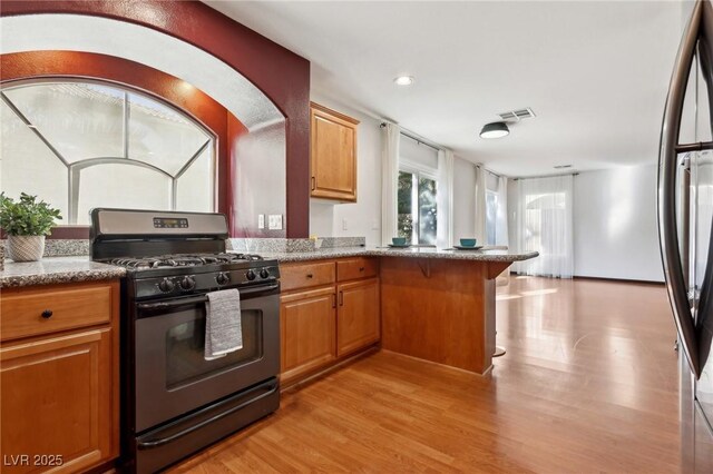 kitchen featuring light stone countertops, range with gas cooktop, kitchen peninsula, and light hardwood / wood-style flooring