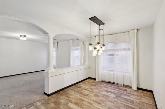 unfurnished dining area featuring decorative columns, light hardwood / wood-style floors, and a notable chandelier